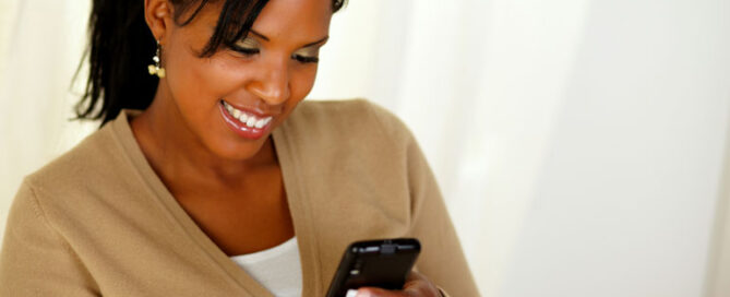 Woman is smiling while looking at her smartphone.