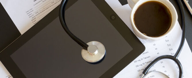 A stethoscope resting on an iPad, with a cup of coffee beside it.