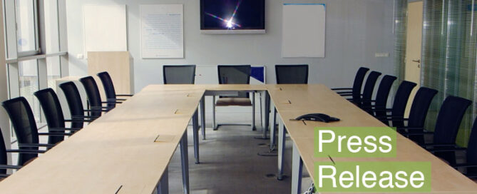 A conference room with a long table and several black chairs with text "Press Release".