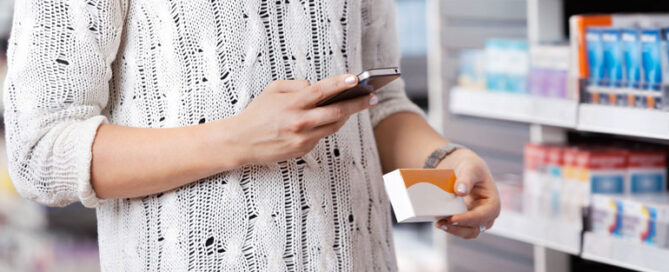 Person standing in a store aisle, holding a smartphone and a small box.