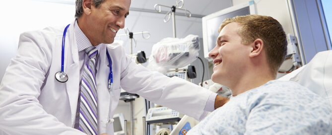 Doctor is smiling and shaking hands with a patient lying in a hospital bed.