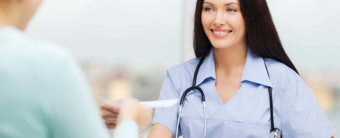 Female healthcare professional smiling while sitting at a table, facing another person.