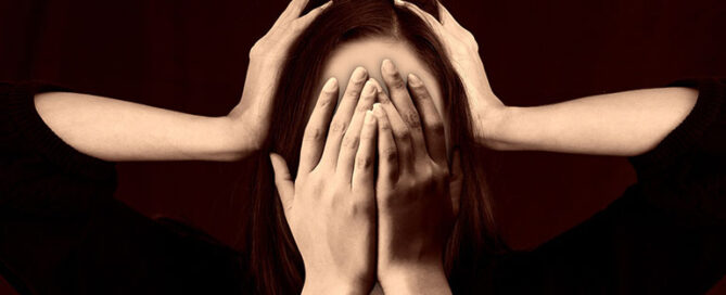 Person with their hands covering their face, a gestures suggests feelings of distress or overwhelm.