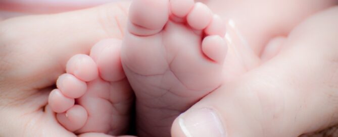 A close-up of a small baby's foot being gently held by an adult's hands.