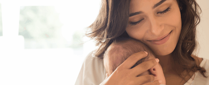 Woman holding a baby close to her face, smiling warmly while expressing affection.