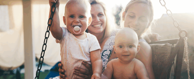 Two small children, surrounded by their mothers, who are smiling and enjoying the moment.