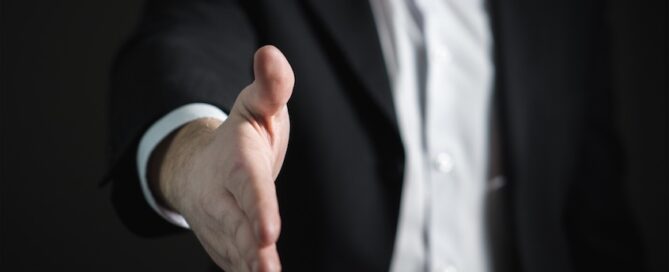A close-up of a man in a suit extending his right hand for a handshake.