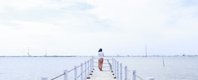A person is walking along a wooden pier that extends into a calm body of water.