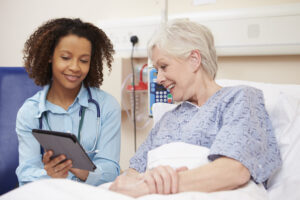 Doctor sitting by female patient's bed using digital tablet.