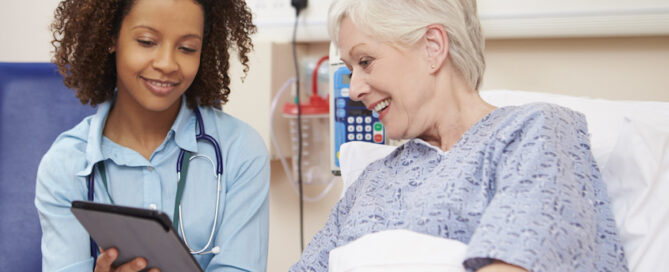 Doctor sitting by female patient's bed using digital tablet.