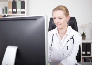 Female Physician with Stethoscope on her Shoulders Looking at the Computer Monitor.