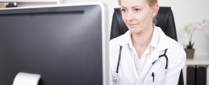 Female Physician with Stethoscope on her Shoulders Looking at the Computer Monitor.
