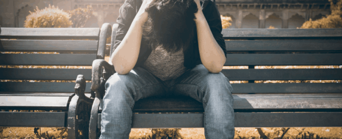 A person sitting on a bench with their head down, appears to be in distress or deep thought.