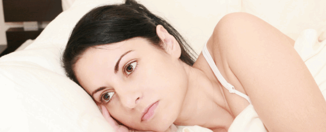 Woman is lying on a bed, resting her head on her hand with a pensive expression.