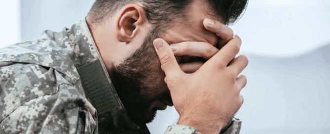 Man in military uniform appears to be distressed, with his hands covering his face.