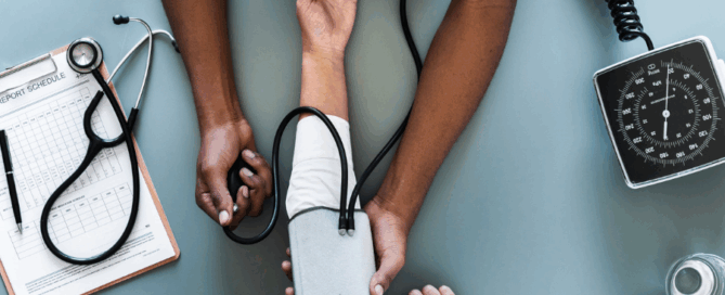 A close-up of two hands measuring blood pressure on an arm, along with a clipboard containing medical charts.