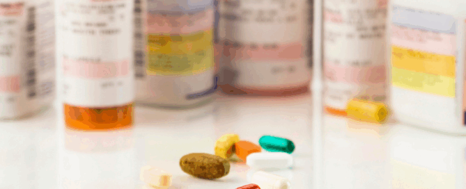 A collection of prescription medication bottles in the background, with several colorful pills and capsules placed in front on a reflective surface.