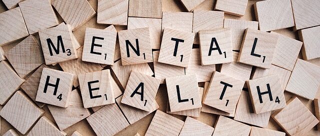 Wooden Scrabble tiles arranged on a surface, spelling out the words "MENTAL HEALTH."