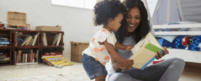 Woman is smiling as she reads from a book, while the child leans in close, showing curiosity and engagement.