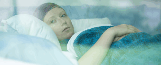 Woman lies propped among white pillows, their head cradled gently as they look out of frame with a steady, contemplative gaze.