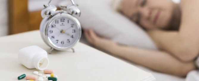 Senior woman sleeping in bed with clock and pills in focus on a side table.