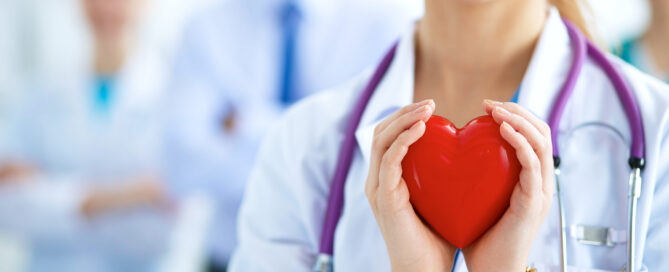 Female doctor holding a red heart shape with both hands.