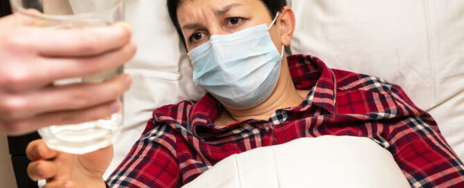 Woman lying in bed, wearing a mask and looking concerned.