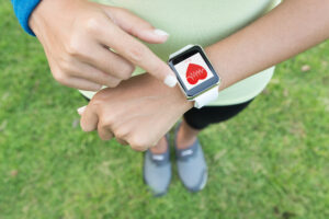 Person is pointing at a smartwatch on their wrist. The watch displays a graphical representation of heart rate data.