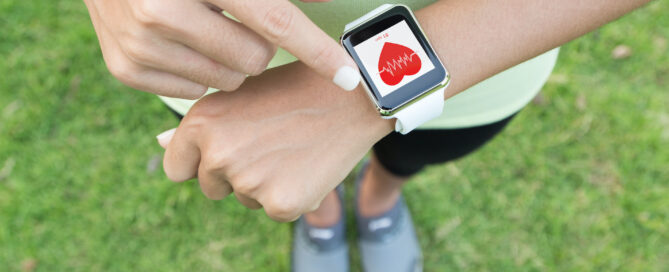 Person is pointing at a smartwatch on their wrist. The watch displays a graphical representation of heart rate data.