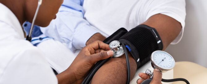 Doctor measuring a patient's blood pressure using a sphygmomanometer and a stethoscope.