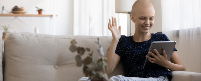 A person with a bald head is sitting on a couch, smiling and holding a tablet, seemingly engaged in conversation or watching something.