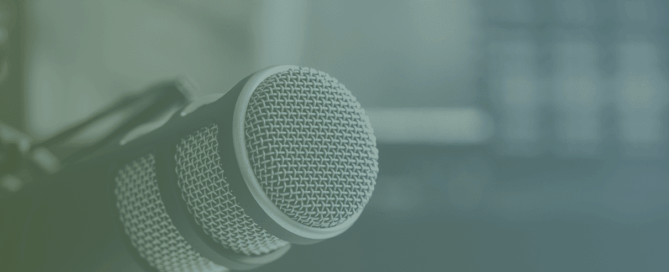 Close-up of a microphone, with a blurred gradient background that suggests an indoor setting.