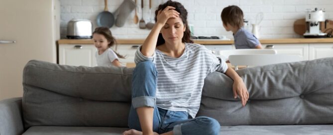 Woman is sitting on a couch, looking stressed or overwhelmed, has her hand on her forehead.