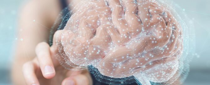 A hand towards a translucent, glowing representation of a brain, which is surrounded by light and sparkling particles.