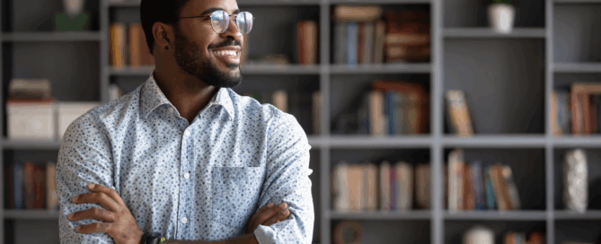 Smiling man with glasses stands with his arms crossed, looking to the side.