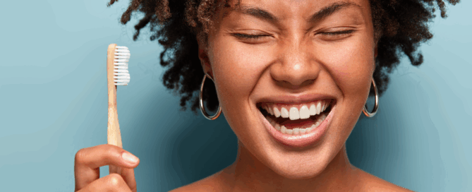 Woman holds a toothbrush in one hand, appears to be enjoying the moment, showcasing her bright smile.
