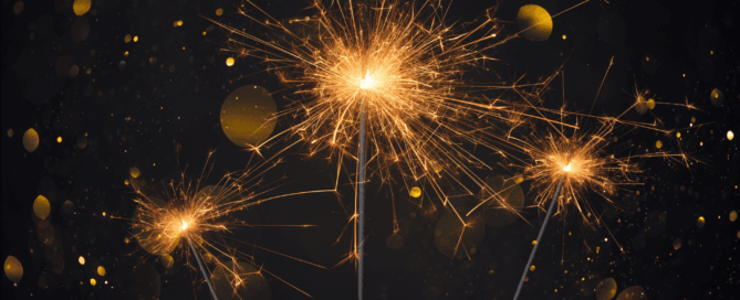 Three sparklers emitting bright golden sparks against a dark background.