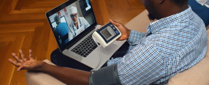 High angle view of African-American man with blood pressure meter consulting doctor online on laptop. Sick guy measuring blood pressure and consulting cardiology on computer at home.