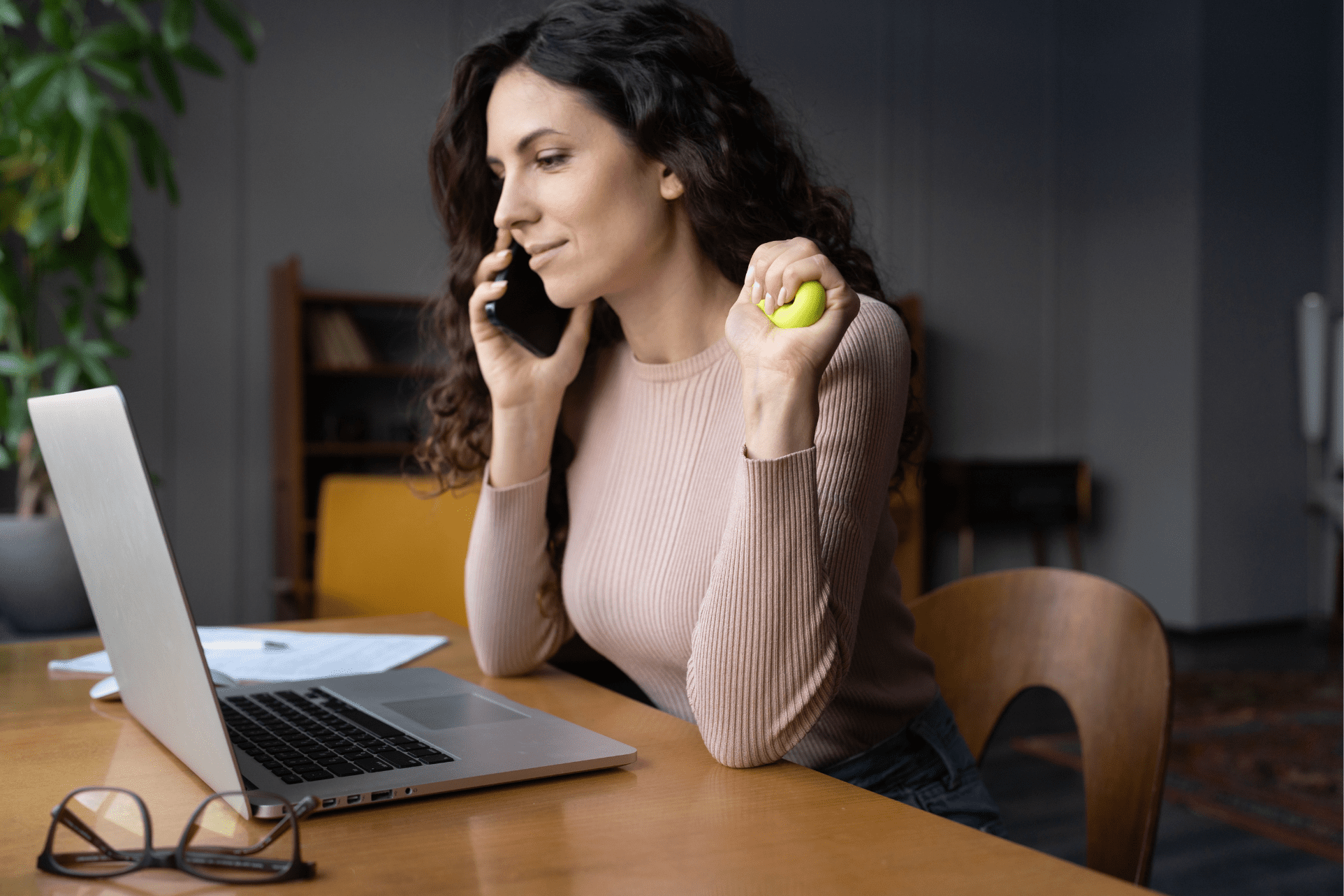 Woman in front of a laptop answering a call on her phone while holding a stress ball