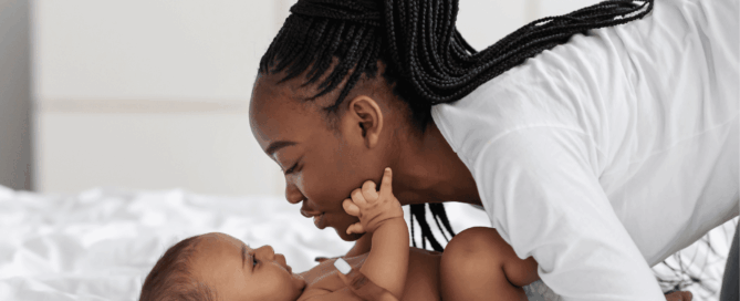 Mother and her baby are lying on a bed, facing each other.