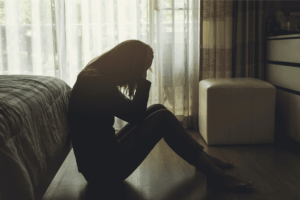 Silhouetted figure of a woman sitting on the floor, appearing distressed.