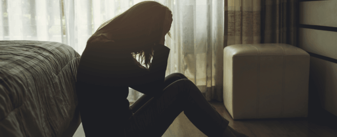 Silhouetted figure of a woman sitting on the floor, appearing distressed.