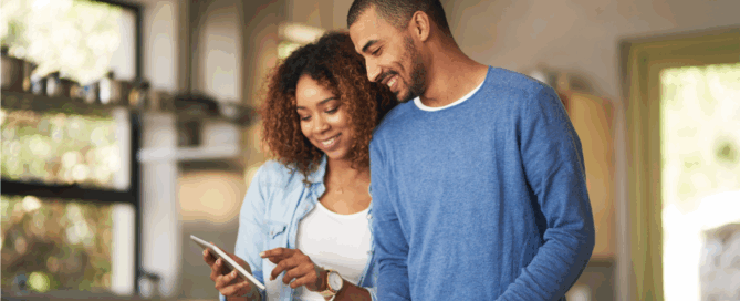 Man and a woman are in a kitchen, looking at a tablet together.