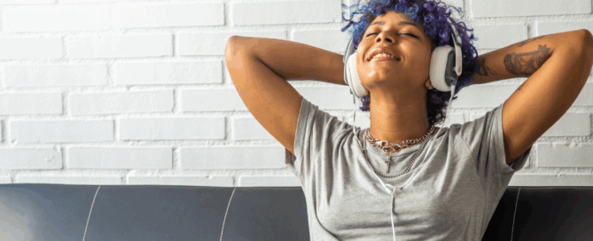 Woman is sitting on a couch wearing headphones, seemingly enjoying the music.