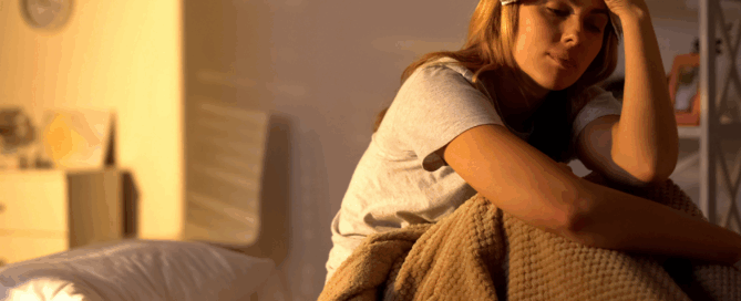 Woman sitting on a bed, appears to be feeling distressed.
