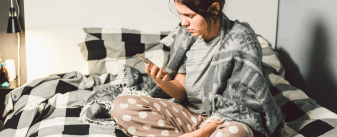Woman is sitting on a bed using a smarthphone.