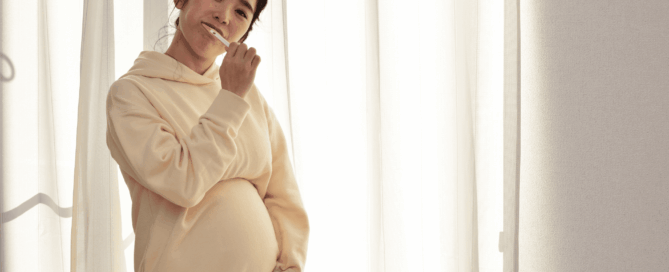 A pregnant standing against a backdrop curtains, smiling and holding a toothbrush.