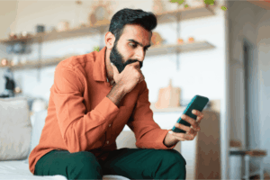 Man is sitting on a couch, looking at his smartphone.