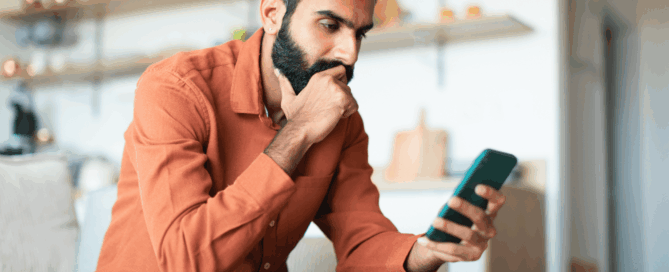 Man is sitting on a couch, looking at his smartphone.