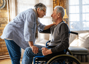 An older woman is leaning in towards an elderly man who is seated in a wheelchair.